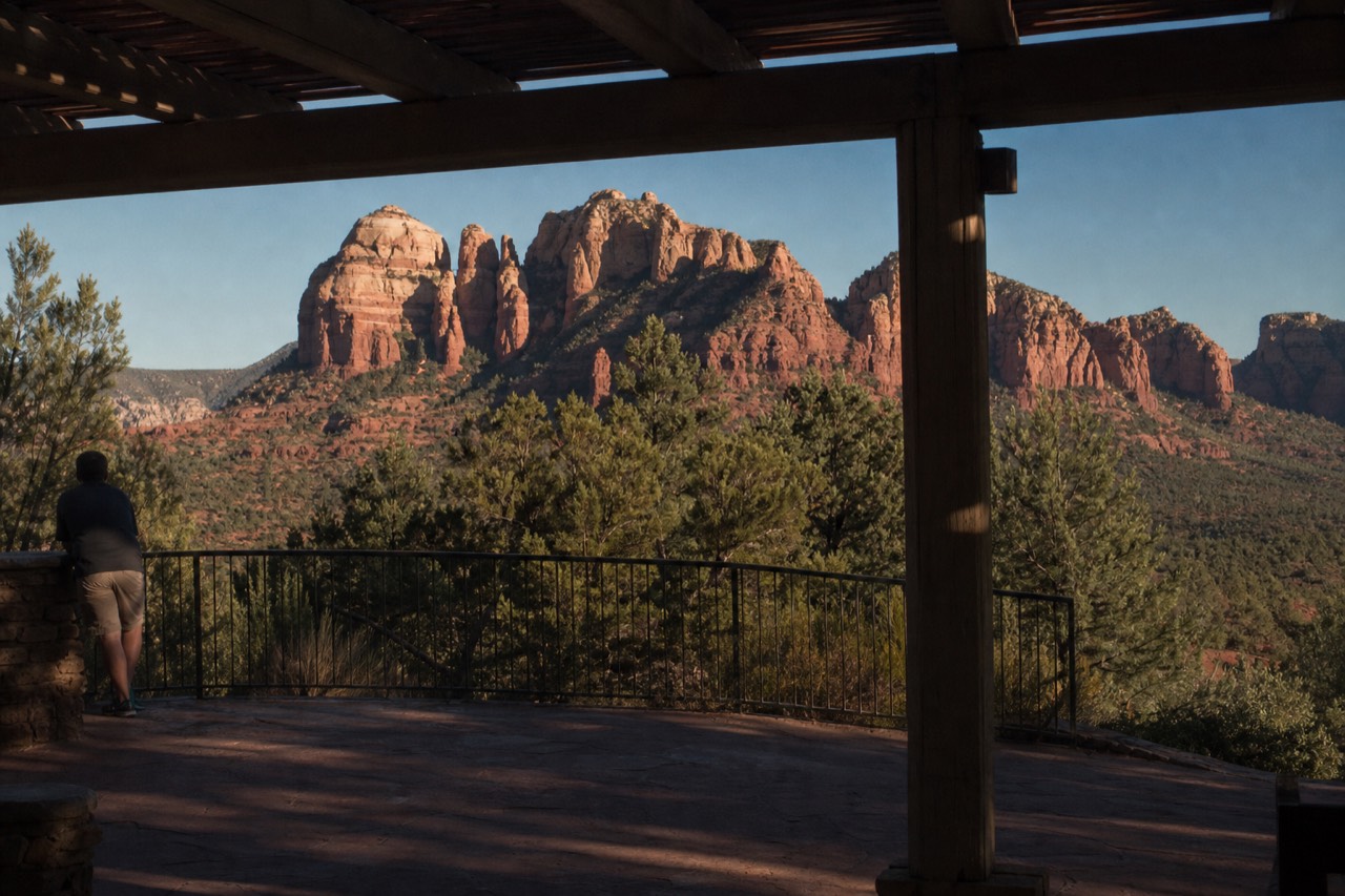 Late afternoon light on Sedona's red sandstone spires seen from a paved overlook, with juniper in the foreground and a clear sky