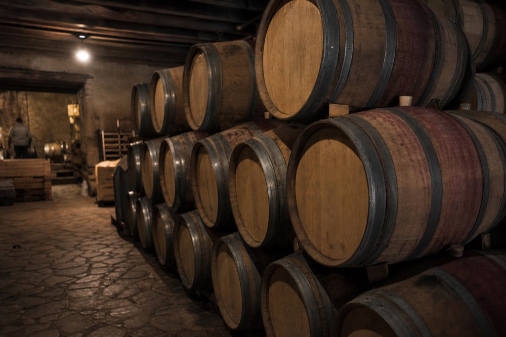 Stacked oak wine barrels in a dim cellar with a single work light overhead and a stone floor