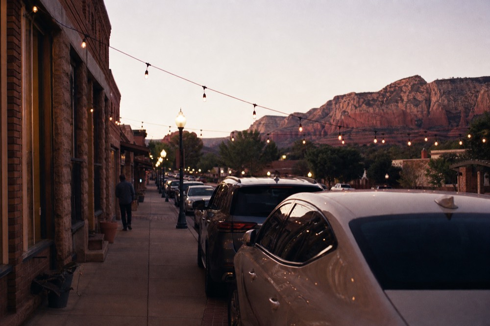 Quiet small-town main street at dusk with brick storefronts, string lights over the sidewalk and parked cars along the curb
