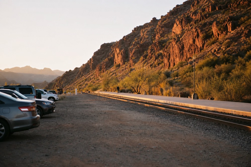 Gravel parking area beside rail tracks at golden hour with a few parked cars and a long low platform