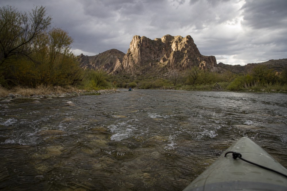 Shallow river water running over pale gravel with small standing waves and a kayak bow entering the frame